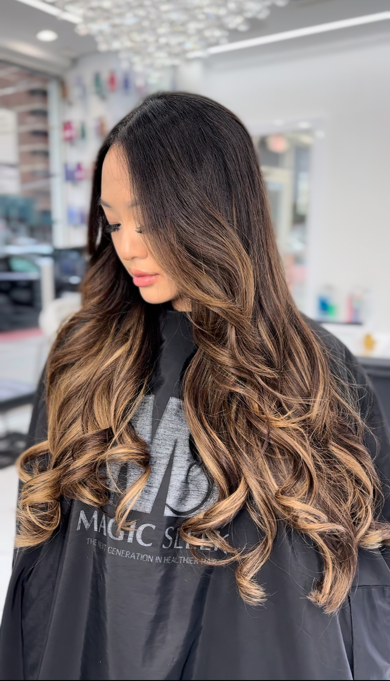 Client wearing a salon cape with long caramel-balayaged extensions