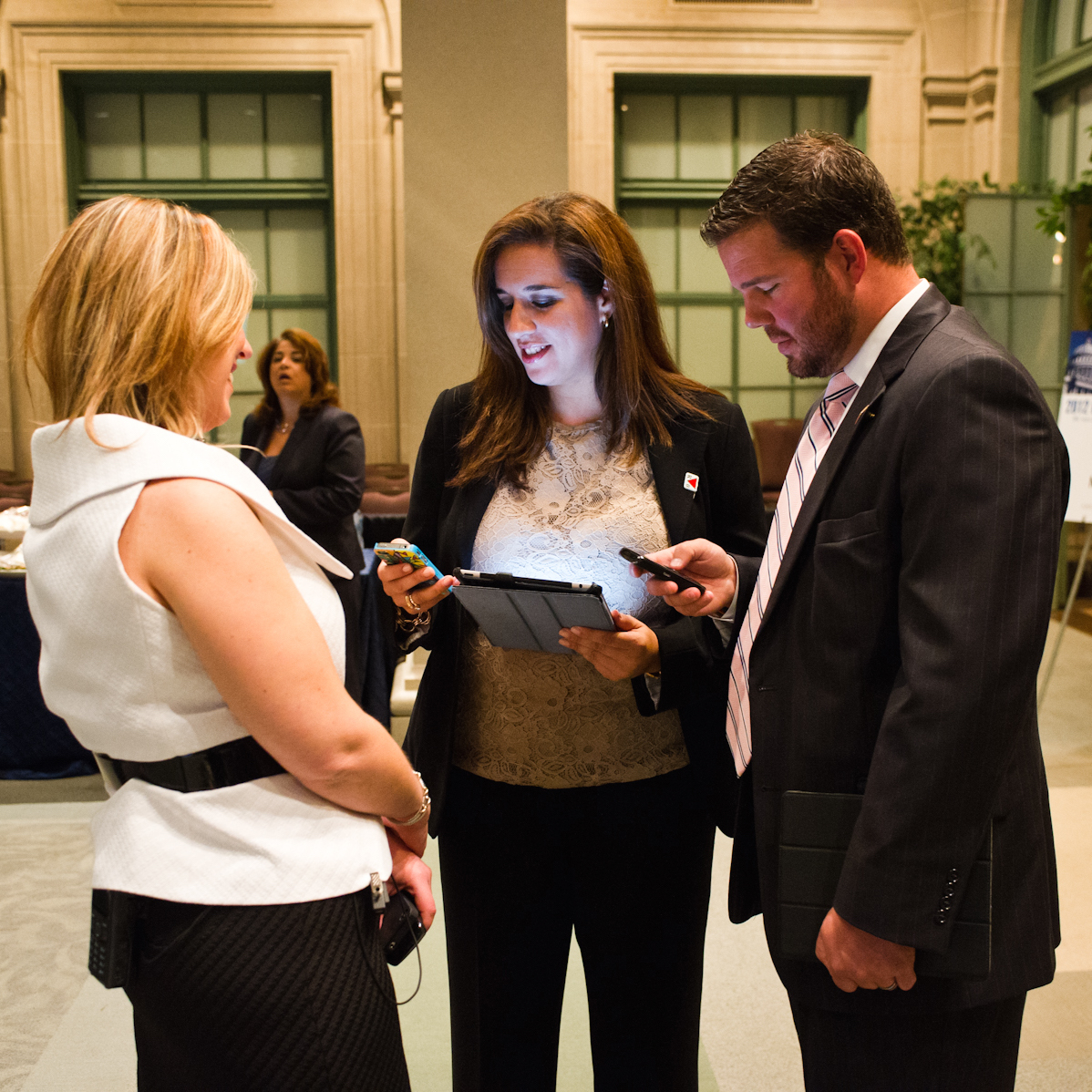 Three professionals at an event, one woman showing content on a tablet to two colleagues
