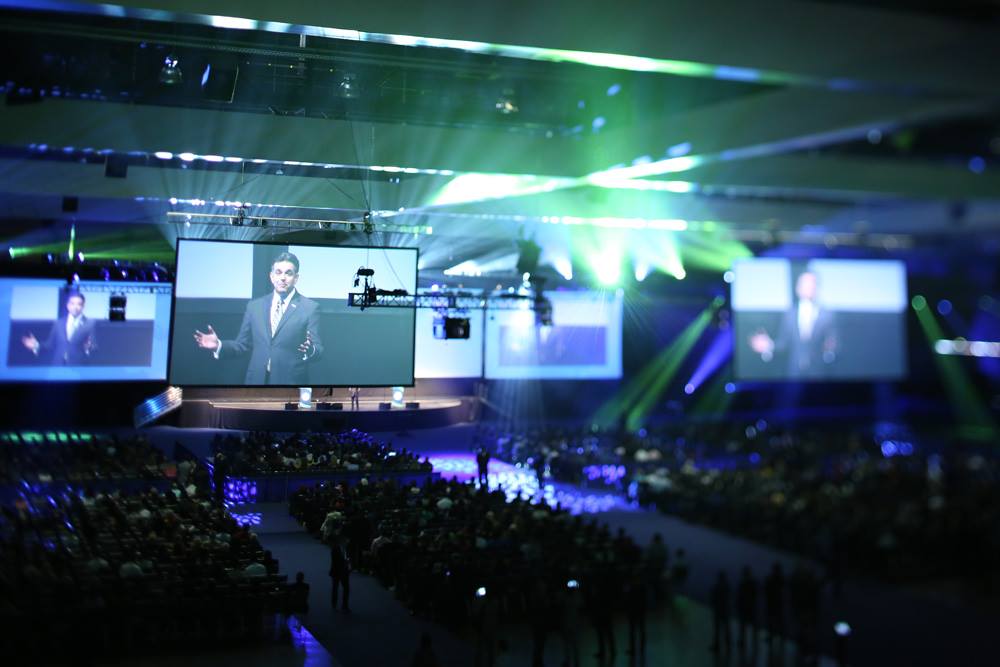 Large-scale conference keynote with giant LED screens and arena-style venue lighting
