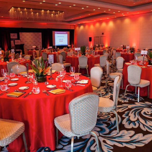 Banquet hall set for a corporate event with red tablecloths, Cisco branding and chandelier lighting