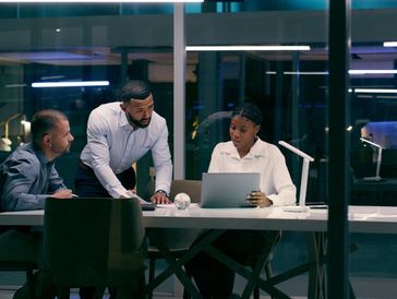 Three business professionals collaborating around a laptop in a dark modern office