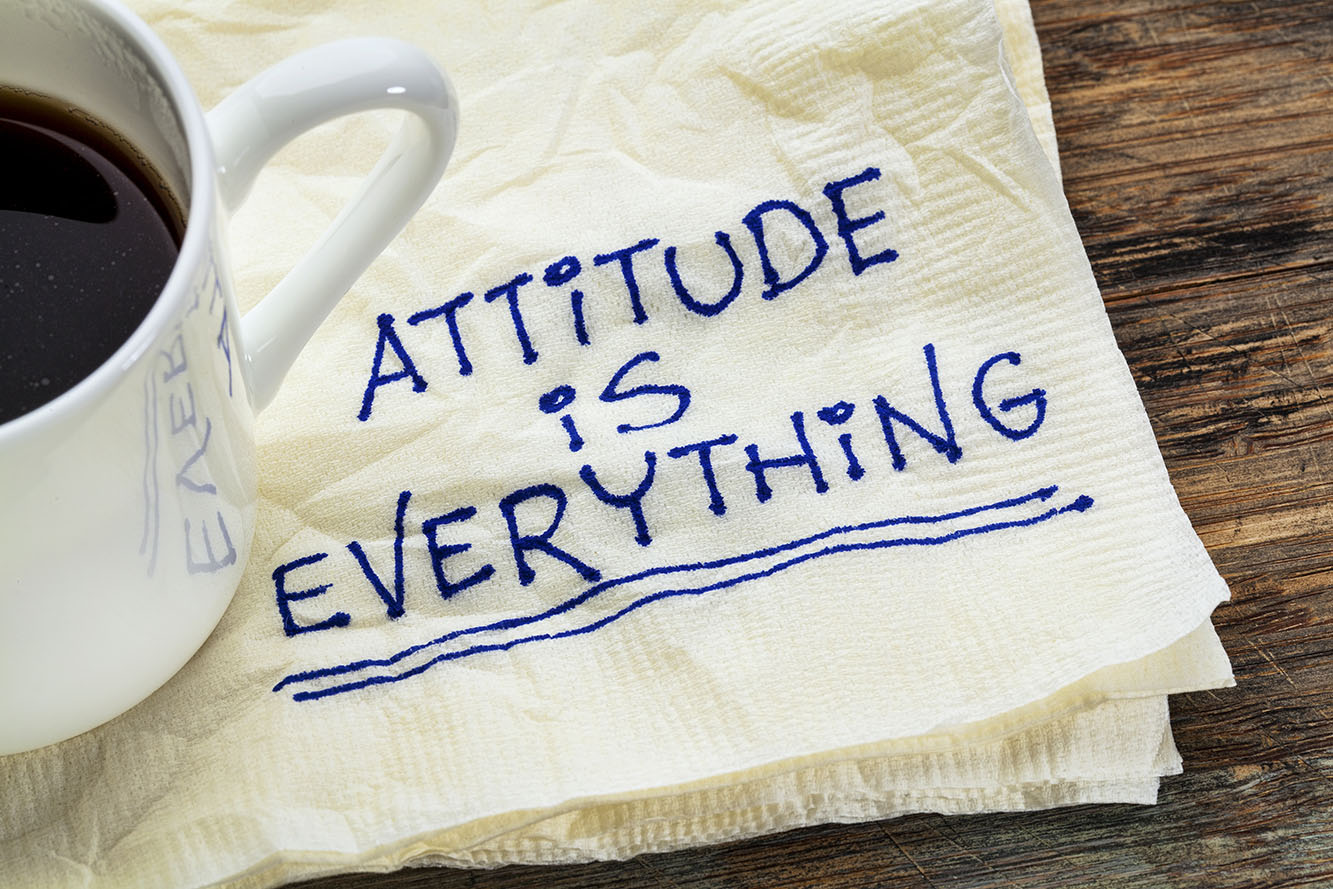 Coffee cup beside a napkin reading Attitude is Everything