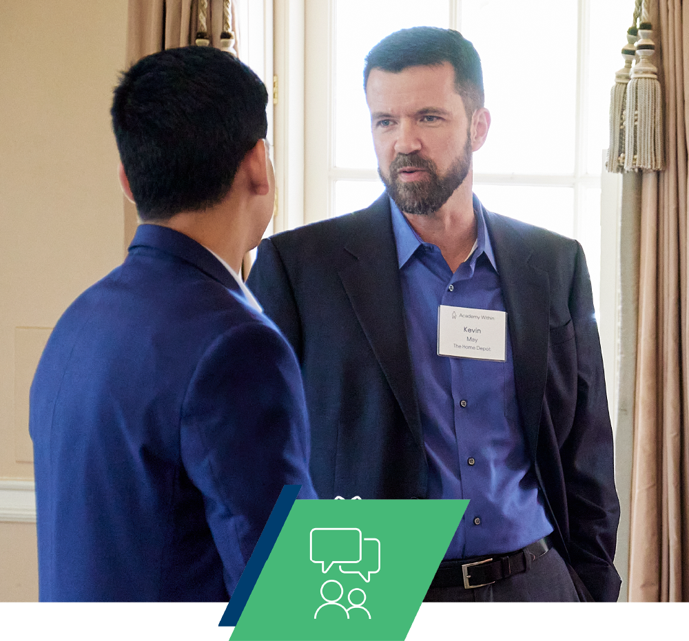 Two men in business attire in conversation, one wearing an Academy Within name badge