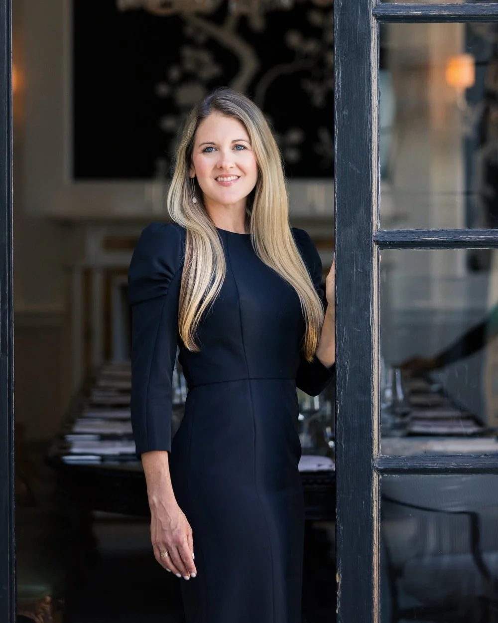 Haley Moore, founder of Acquire, in a black dress in the doorway of an elegant restaurant dining room
