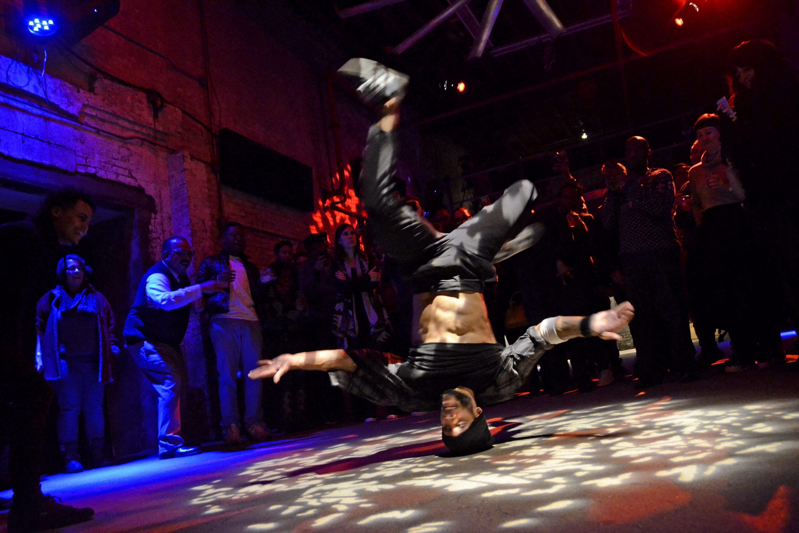 Breakdancer performing a headstand under red and blue stage lighting
