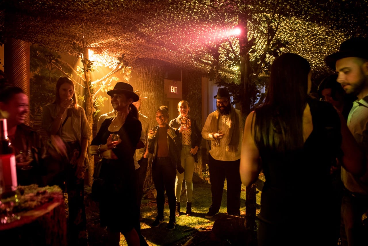 Guests socializing in a forest-themed immersive event with warm amber lighting and ivy canopy