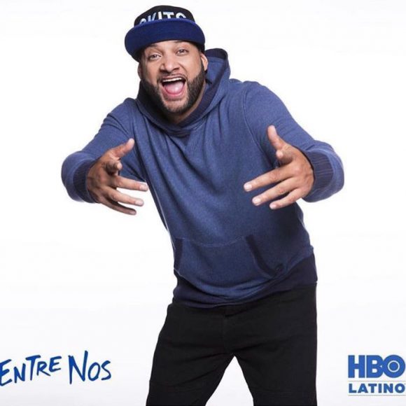 Tonio Skits — comedian in a blue hoodie and cap posing energetically against an HBO Latino Entre Nos backdrop