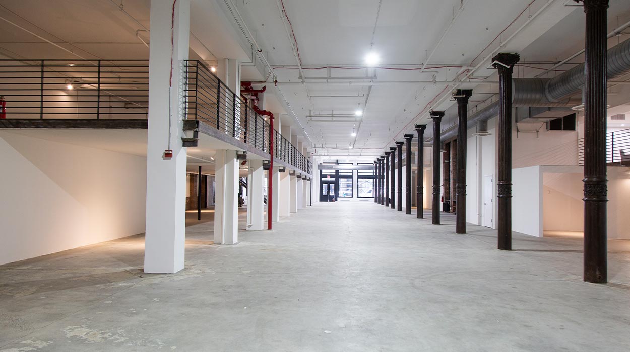 Iron23 empty industrial event hall with ornate dark columns, mezzanine railing and concrete floor
