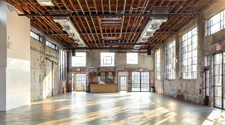 Rustic industrial raw event space with exposed brick, large factory windows and wooden beam ceiling
