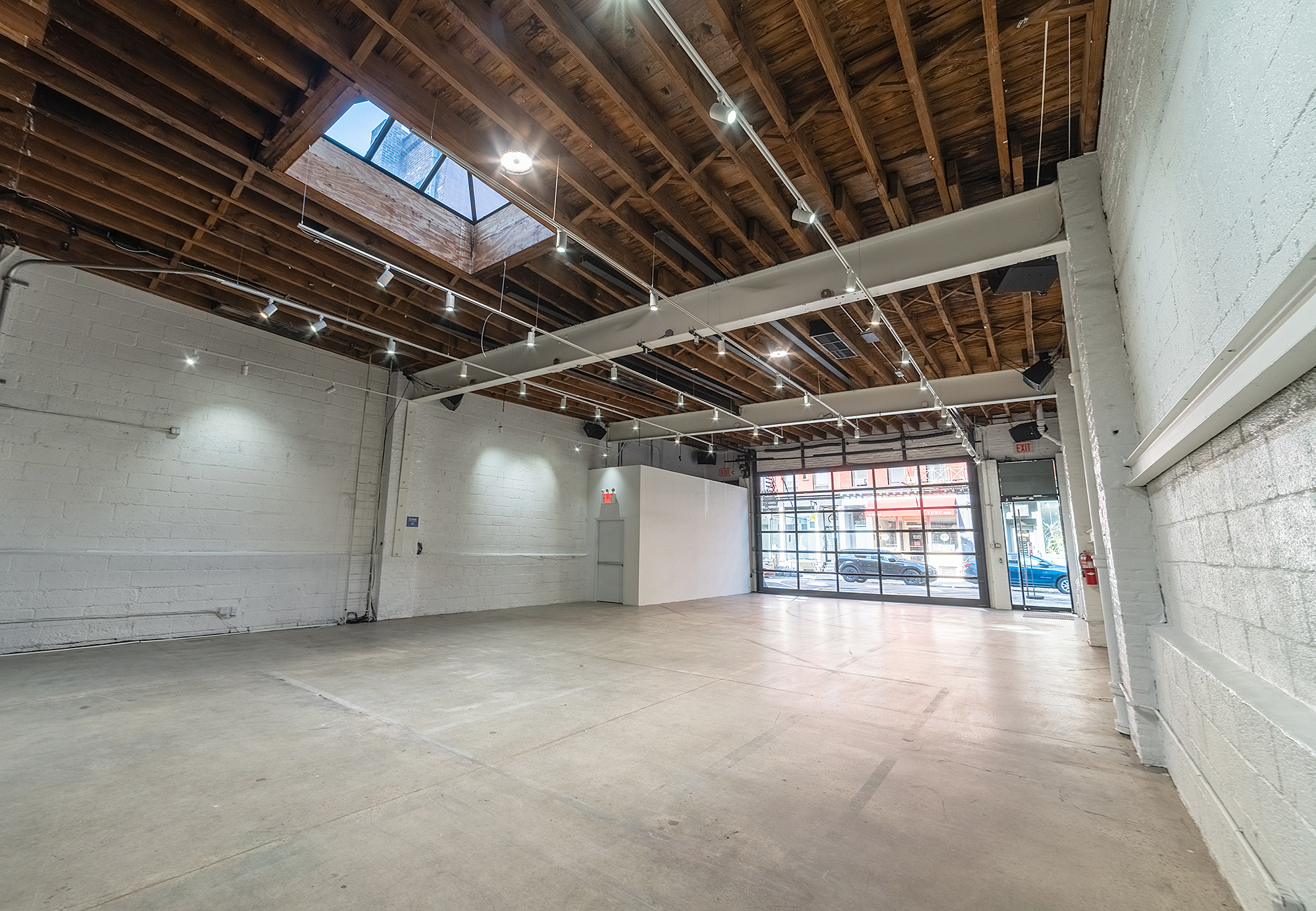 45Grand raw industrial event space with exposed wooden beam ceiling, skylight, concrete floor and garage-door street entrance