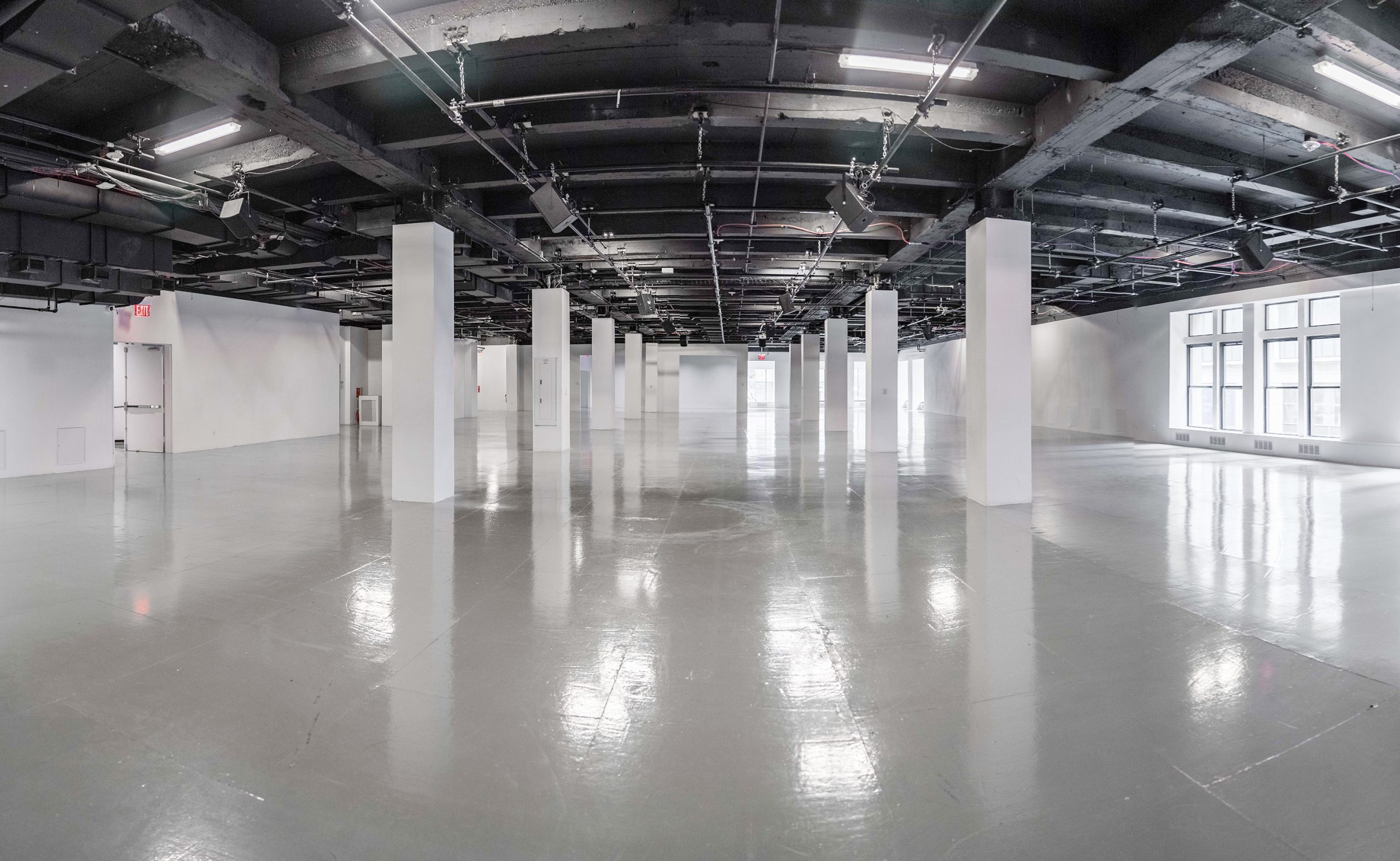 Large empty Center415 event space with black exposed ceiling, white square columns and polished concrete floors