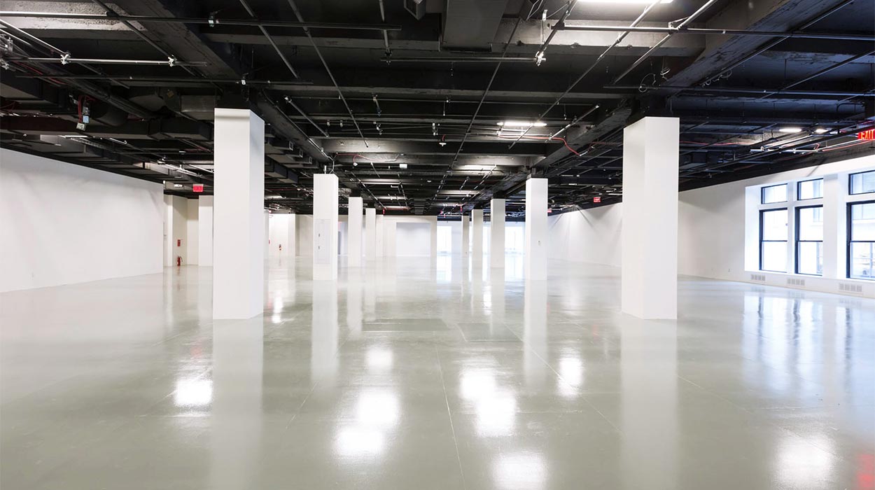 Center415 vast empty event floor with black exposed ceiling grid, white square columns and polished concrete