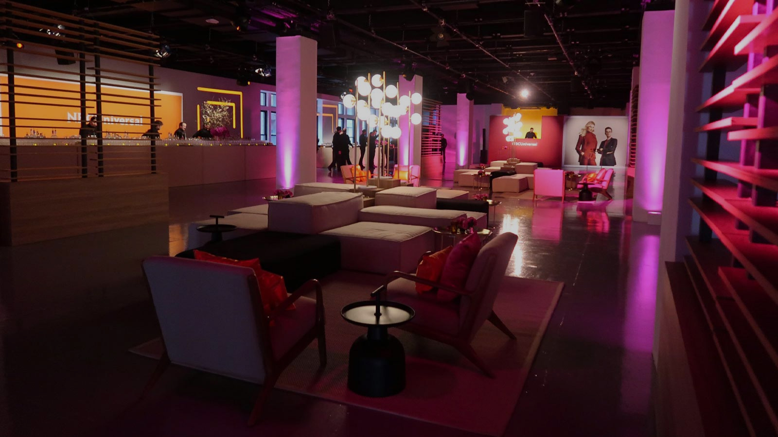 Venue dressed for an NBCUniversal branded corporate event with pink and purple uplighting, lounge seating and bar