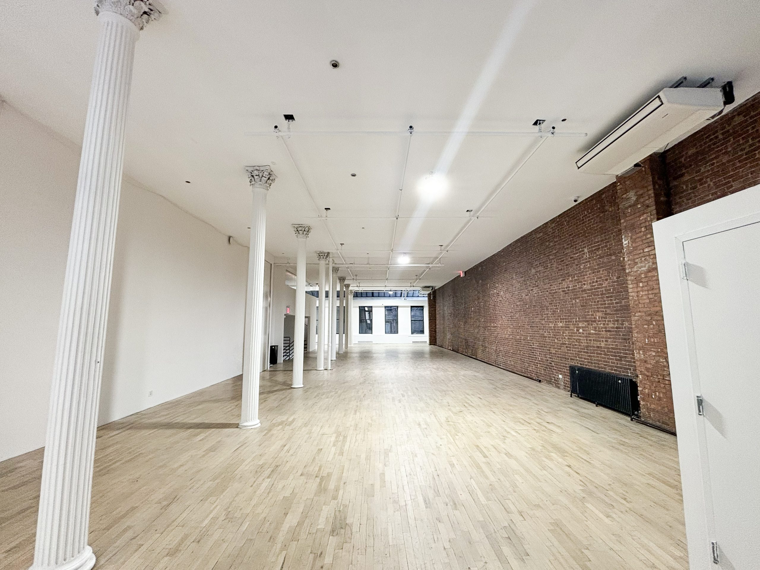 21Greene empty event venue interior with white Corinthian columns, exposed brick wall and light hardwood floors