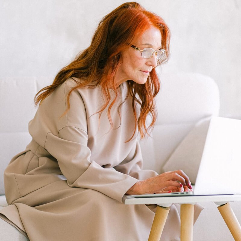 Woman with red hair working on a laptop on a white sofa