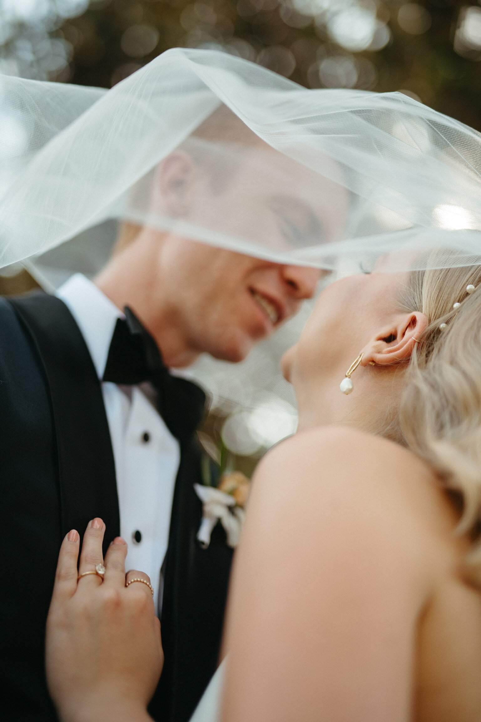 Bride and groom sharing an intimate moment beneath a flowing veil, wedding rings visible