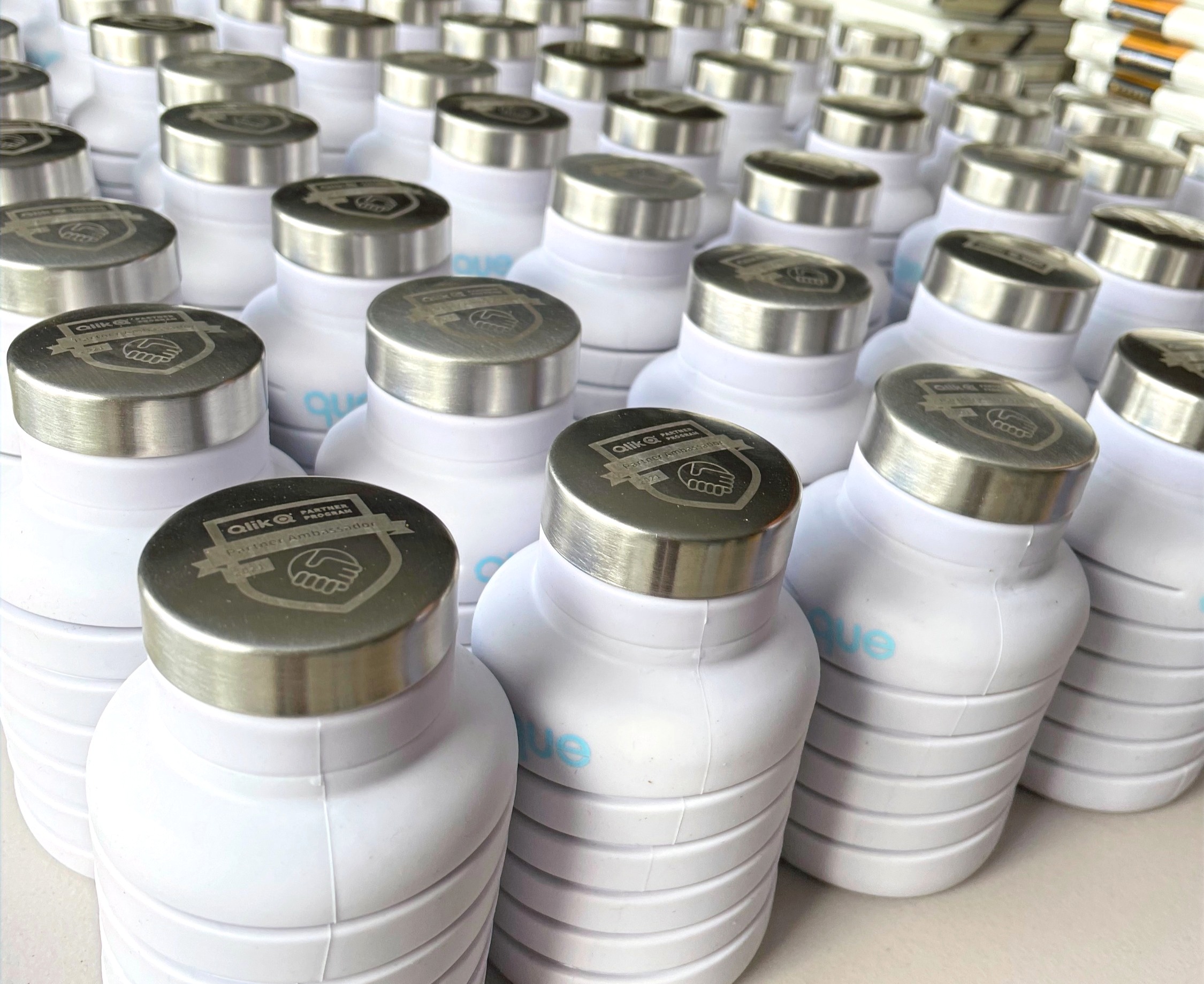 Rows of white Qlik-branded collapsible water bottles with engraved lids