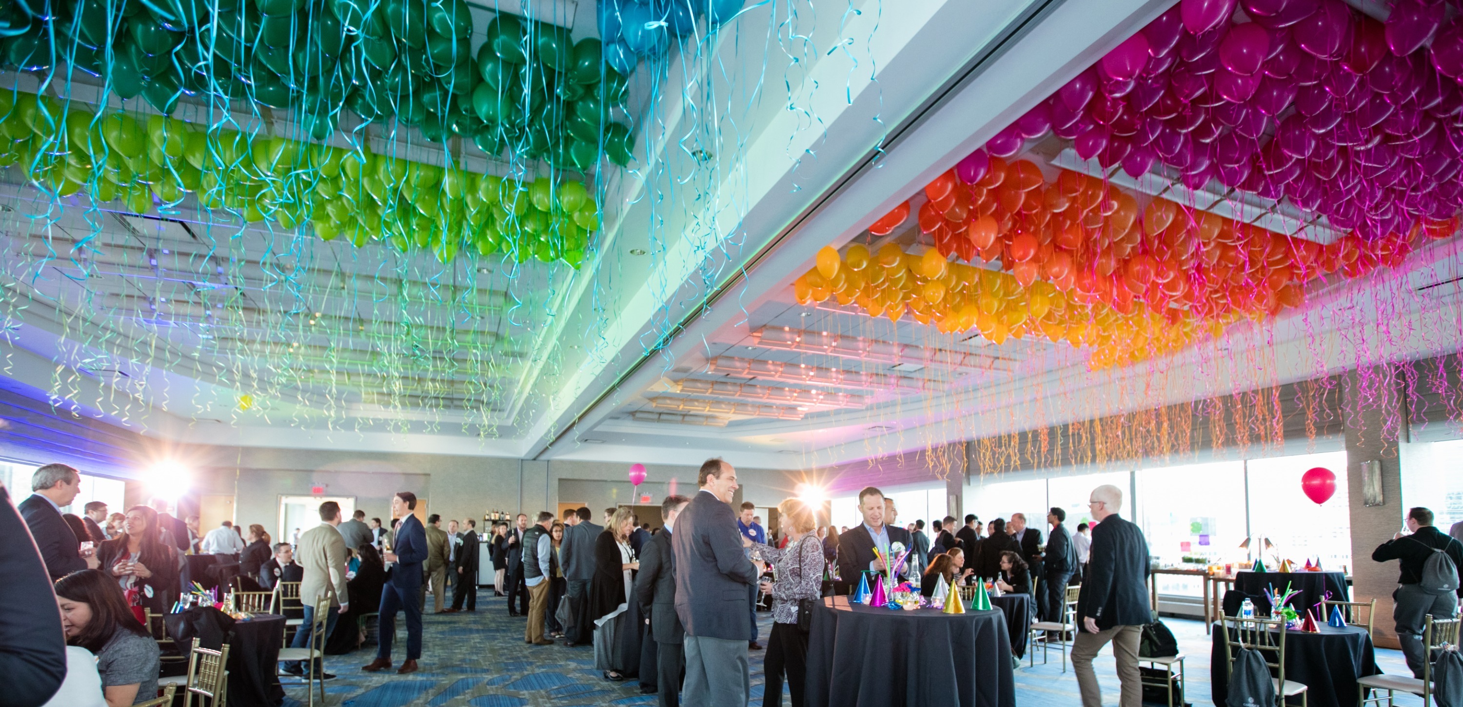 Event hall with a rainbow balloon-ceiling installation and a crowd of attendees