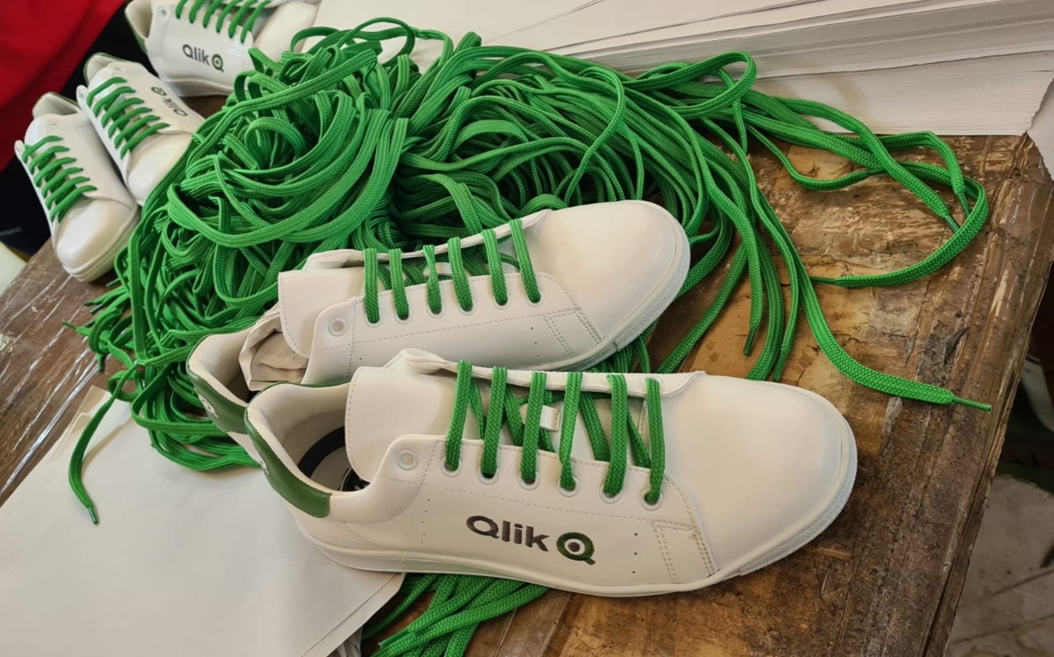 White Qlik-branded sneakers with green laces on a wooden surface