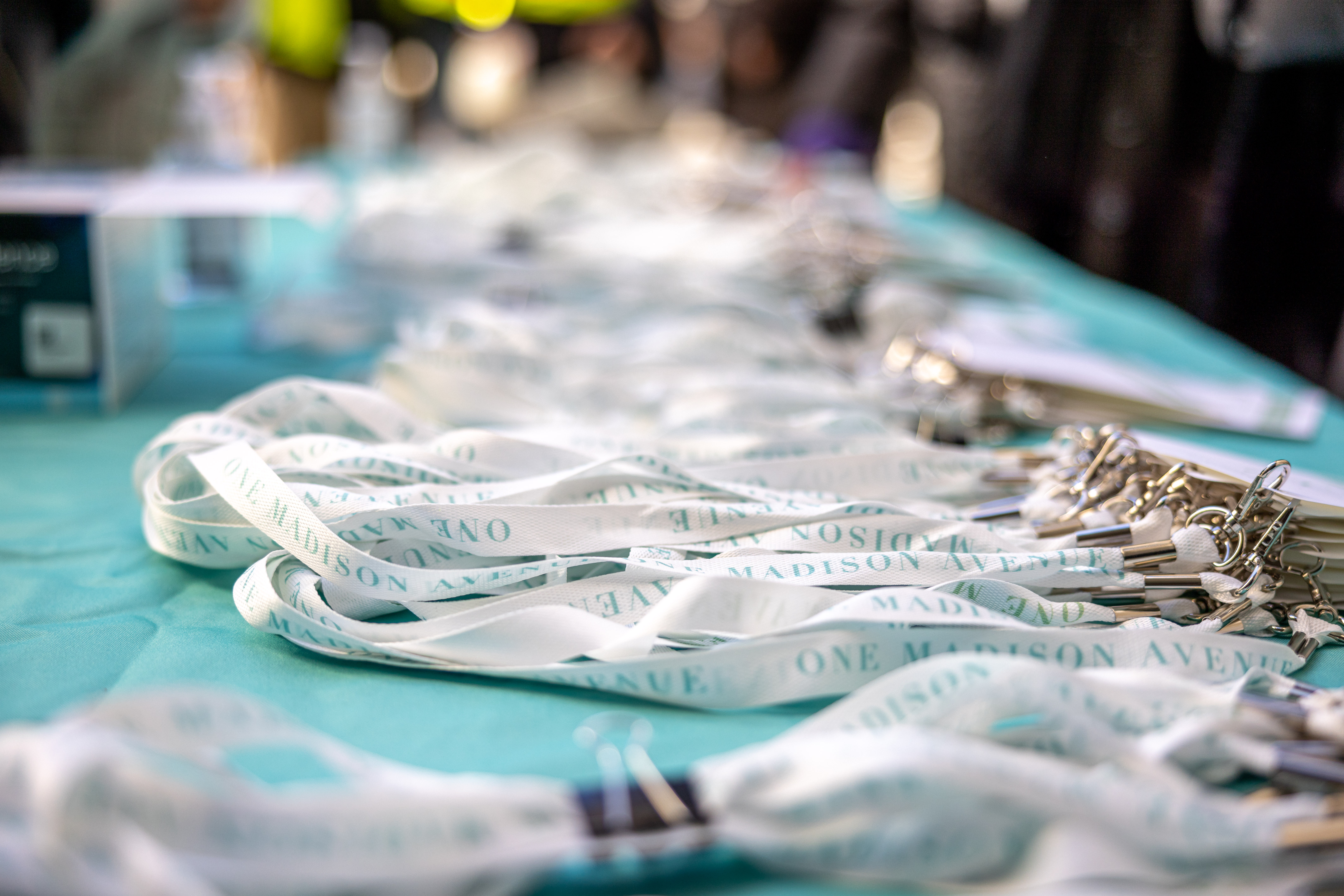 Custom branded lanyards reading 'One Madison Avenue' on a teal event table