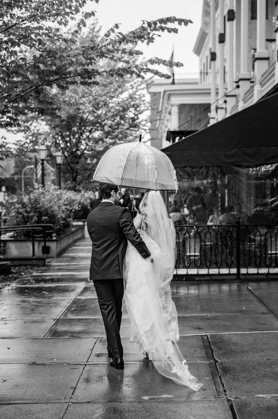 Black and white photo of a bride and groom under a clear umbrella in the rain