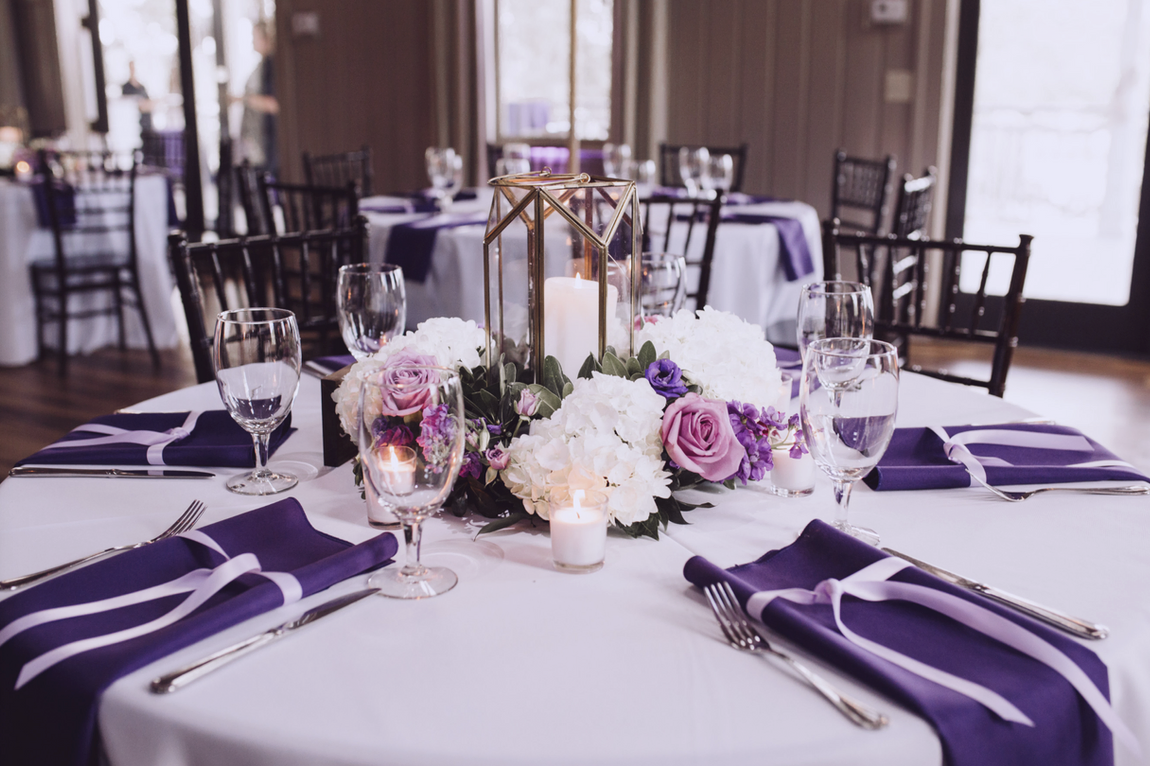 Wedding reception table with purple and white florals in a gold geometric lantern