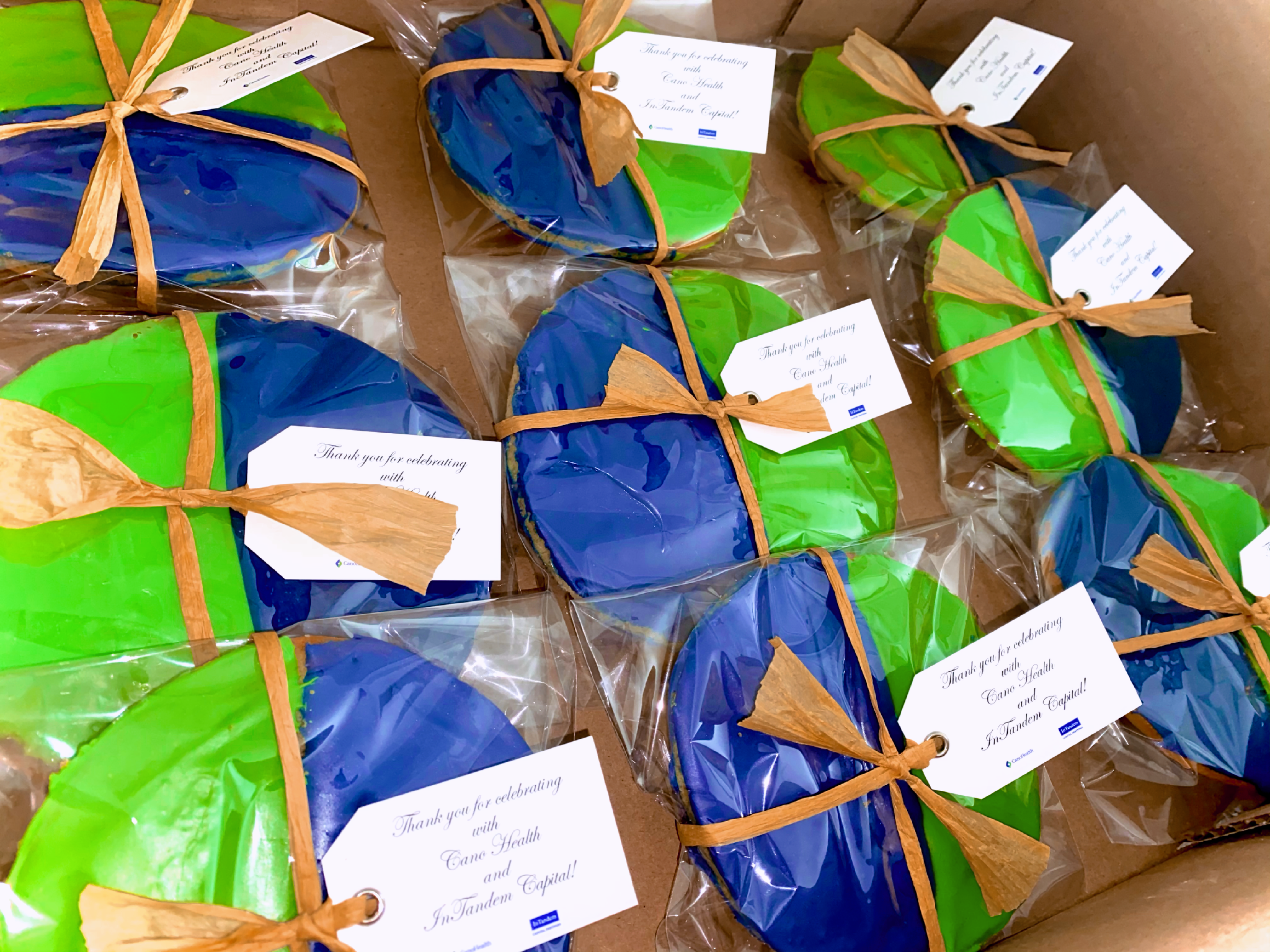 Box of custom branded cookies wrapped in cellophane with raffia bows and gift tags reading 'Thank you for celebrating with Cano Health and InTandem Capital'