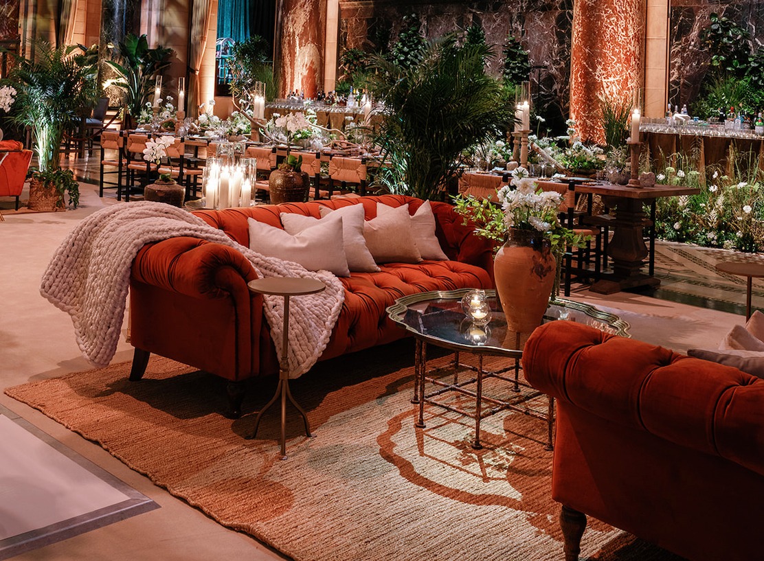 Event lounge with rust-red tufted Chesterfield sofas and ambient lighting