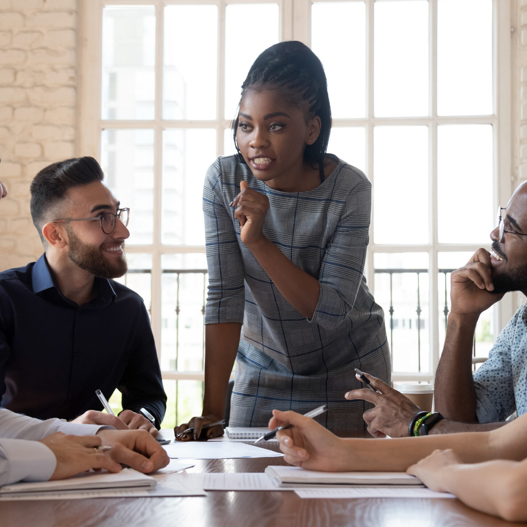 Woman presenting at a table to a small group of diverse colleagues in a bright office