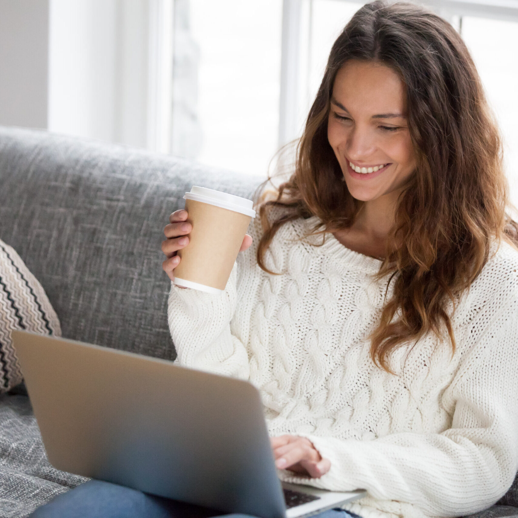 Young woman smiling on a sofa with a laptop and coffee cup