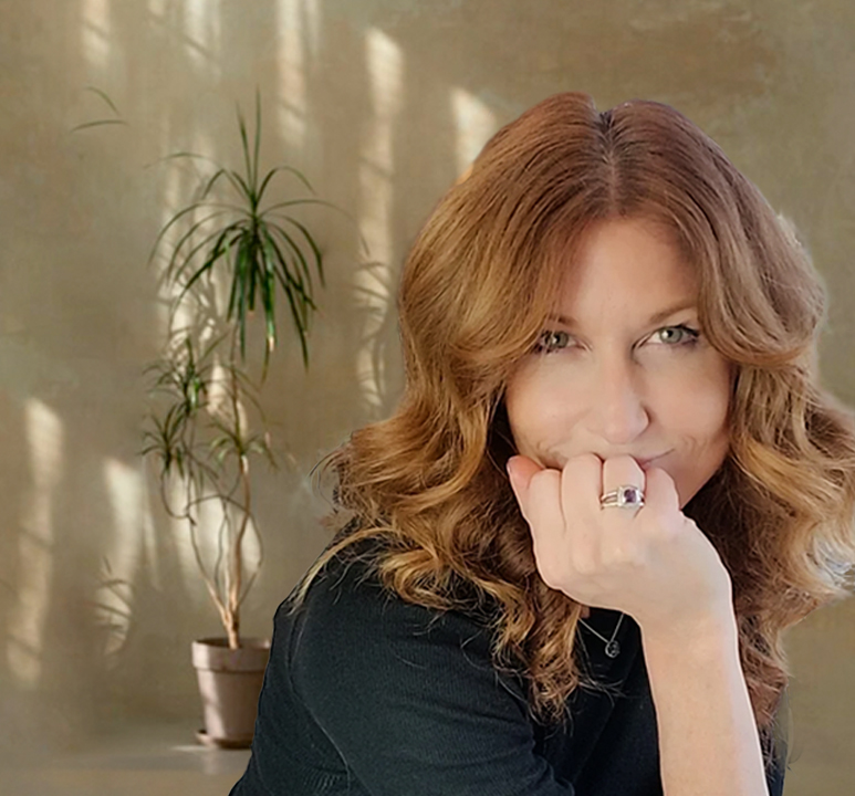 Portrait of Andrea Marcellus, hand to chin, against a warm tan wall with a plant