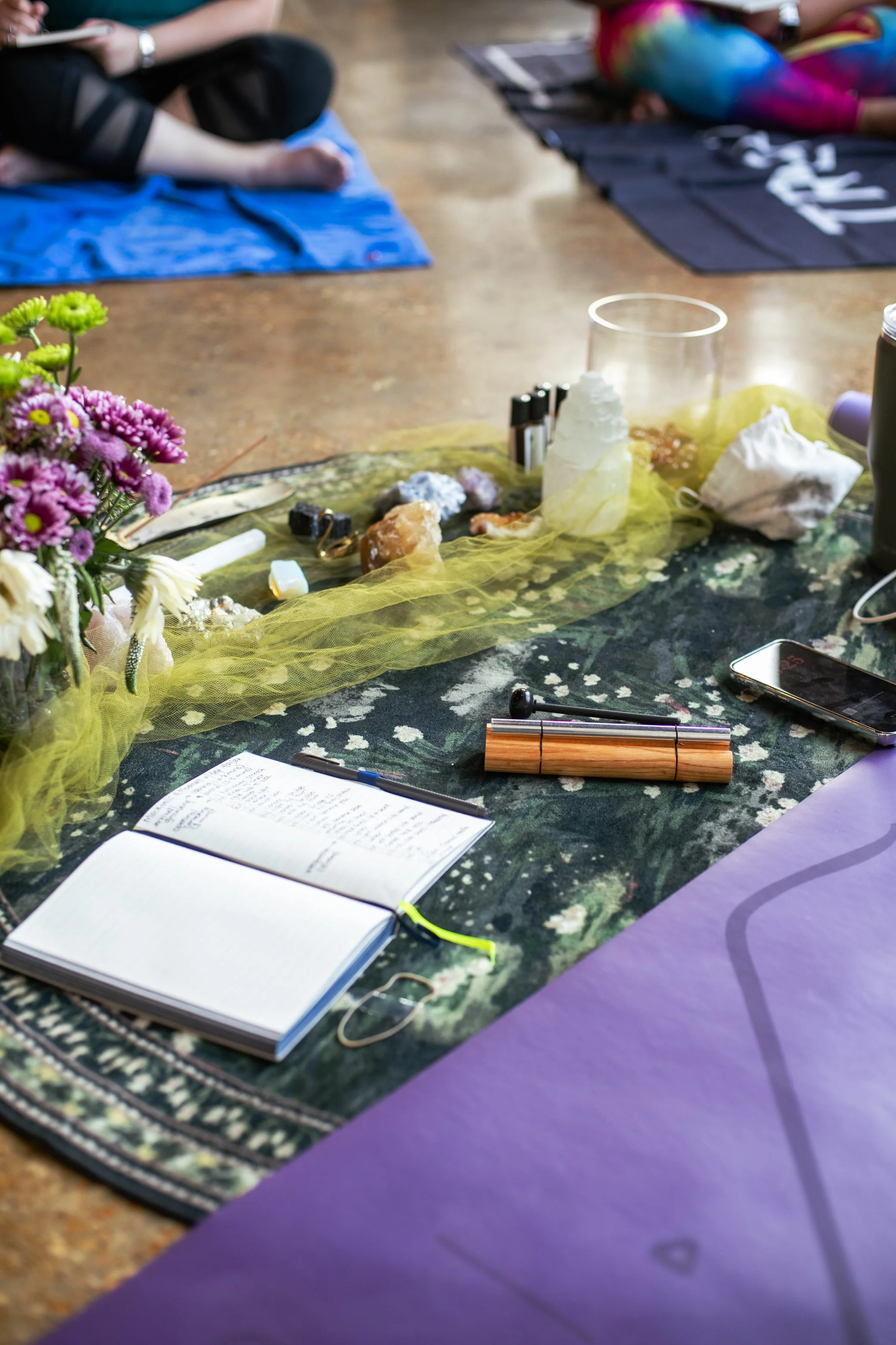 Wellness event floor spread with an open journal, crystals, flowers, candles and yoga mats