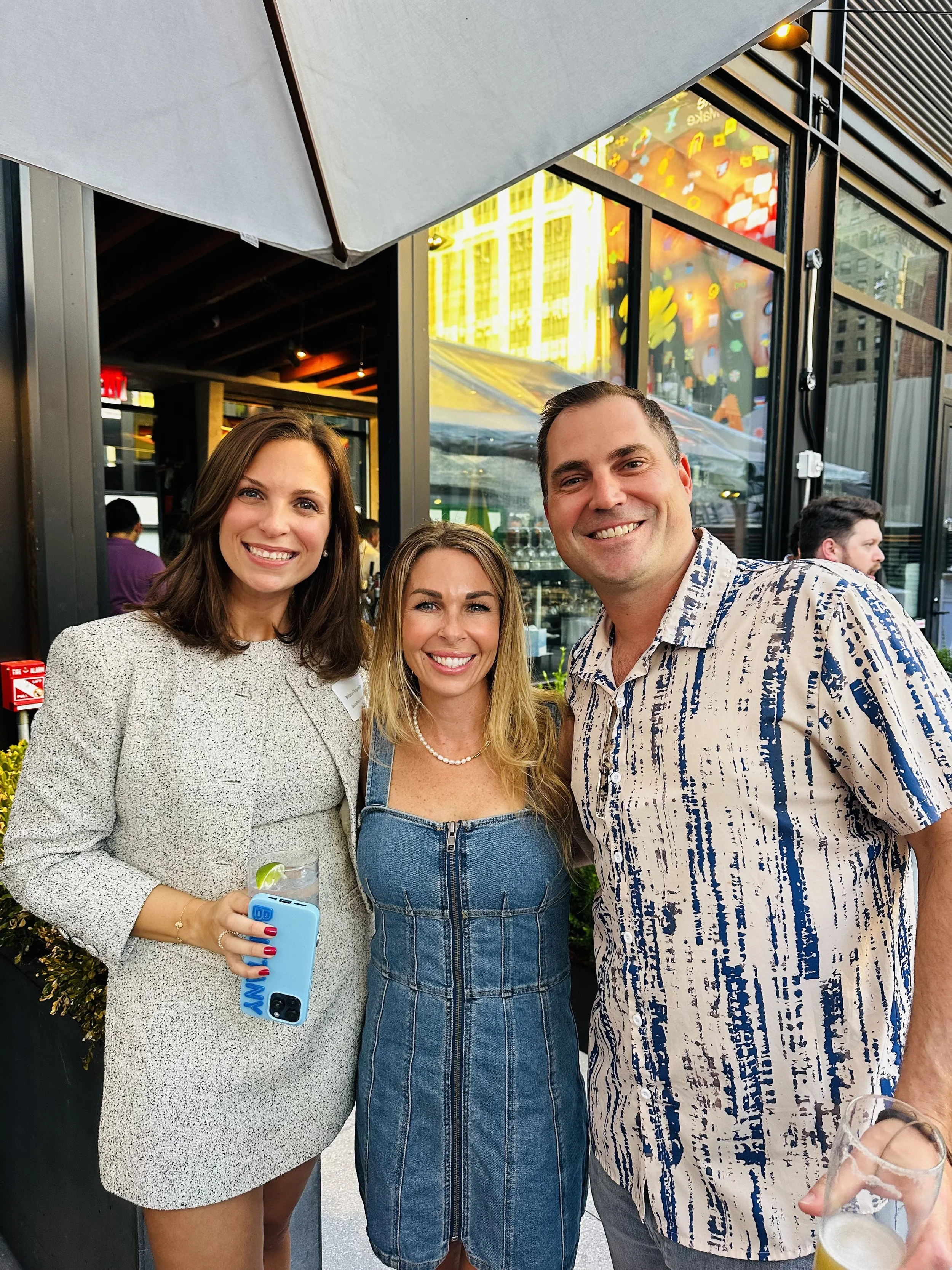 Three people smiling together at an outdoor rooftop bar event
