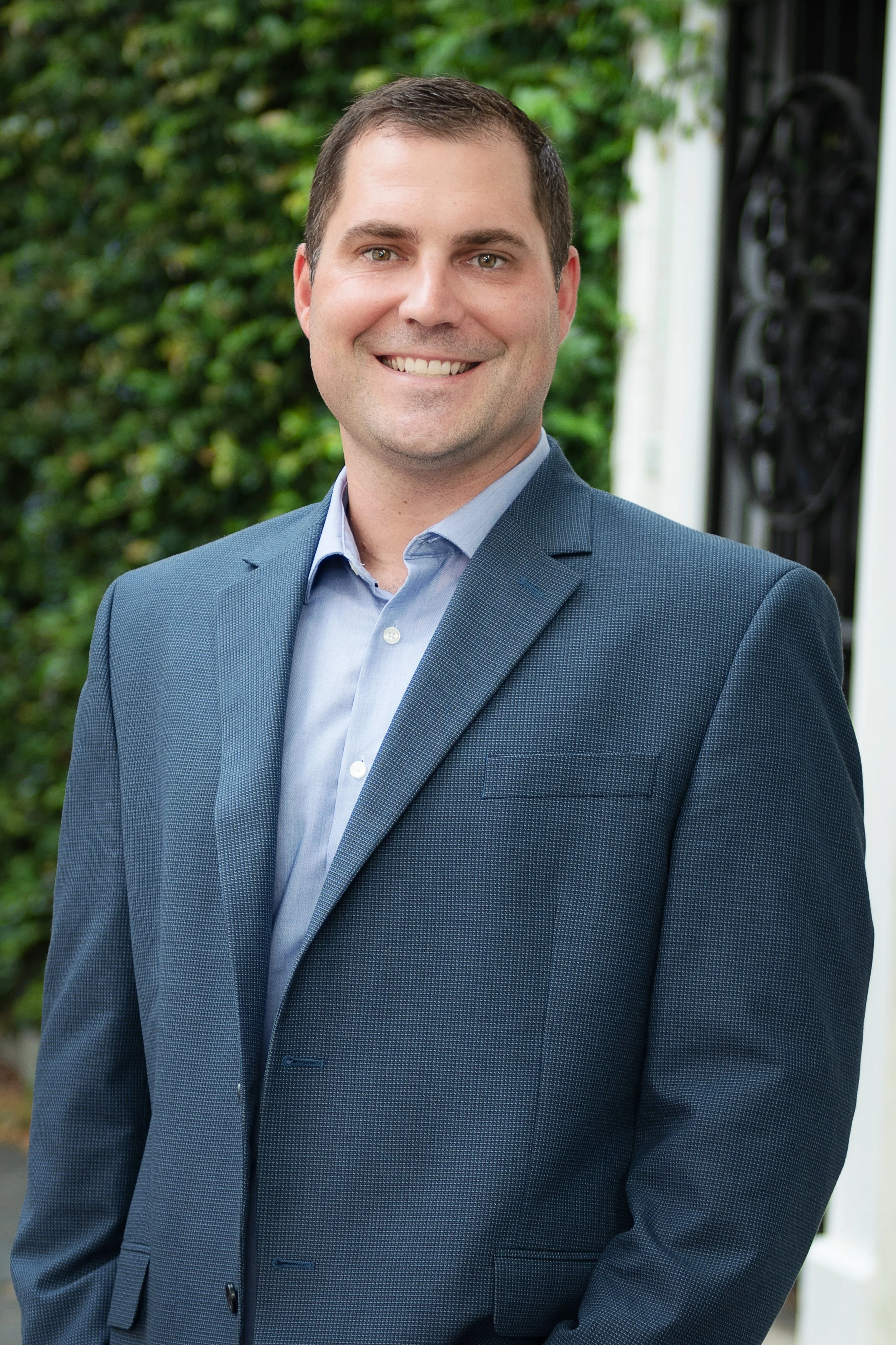 Ryan Kunker in a blue blazer, smiling outdoors against an ivy-covered wall