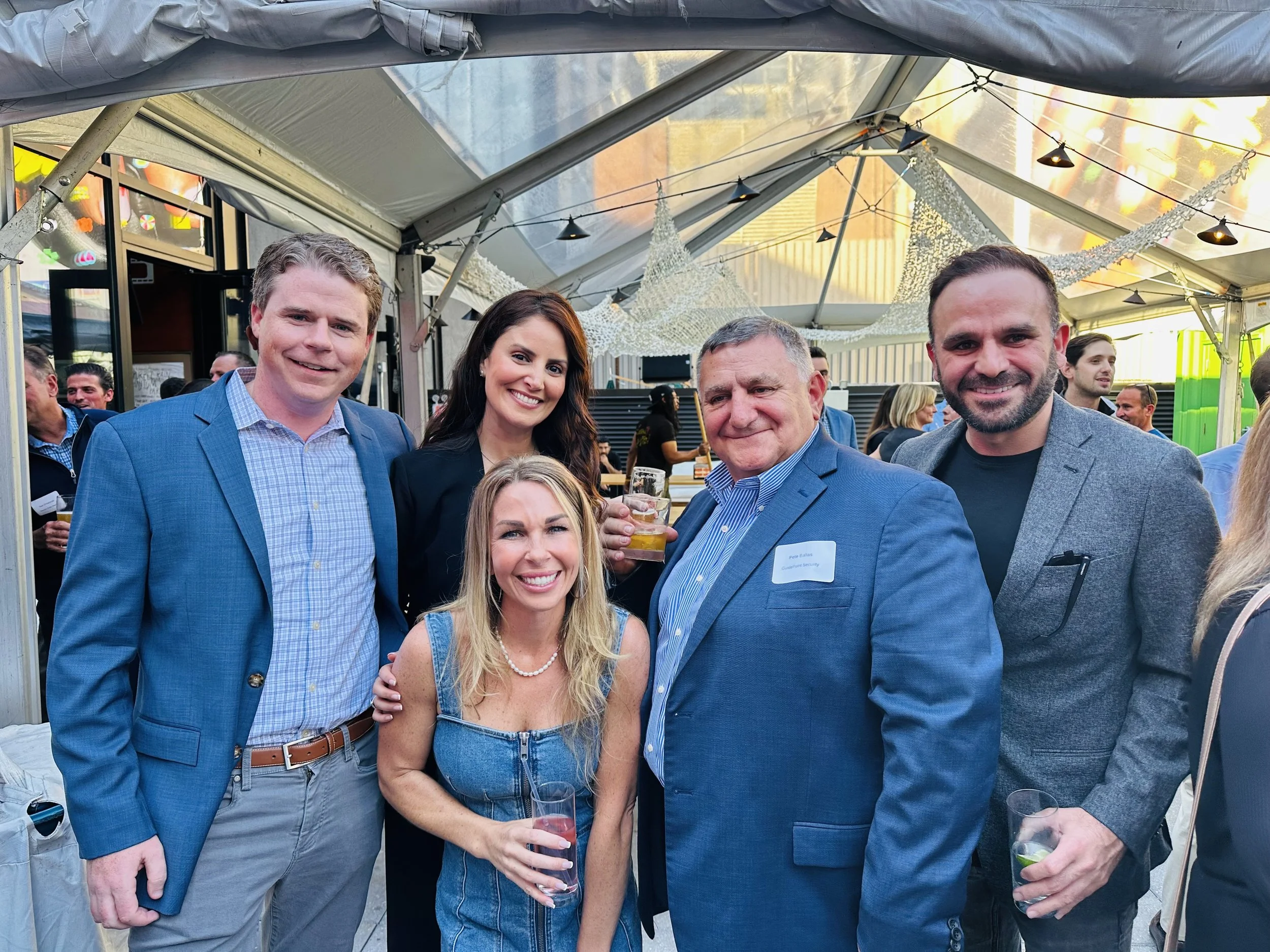 Five people posing at an outdoor industry happy hour under a tent