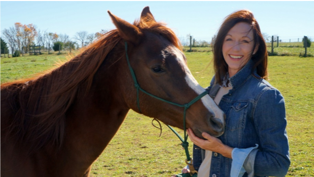 Melba Holliday smiling with a chestnut horse in a field