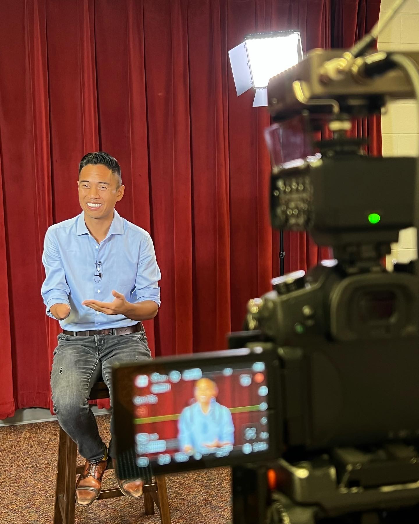 Interview subject being filmed in front of a red curtain