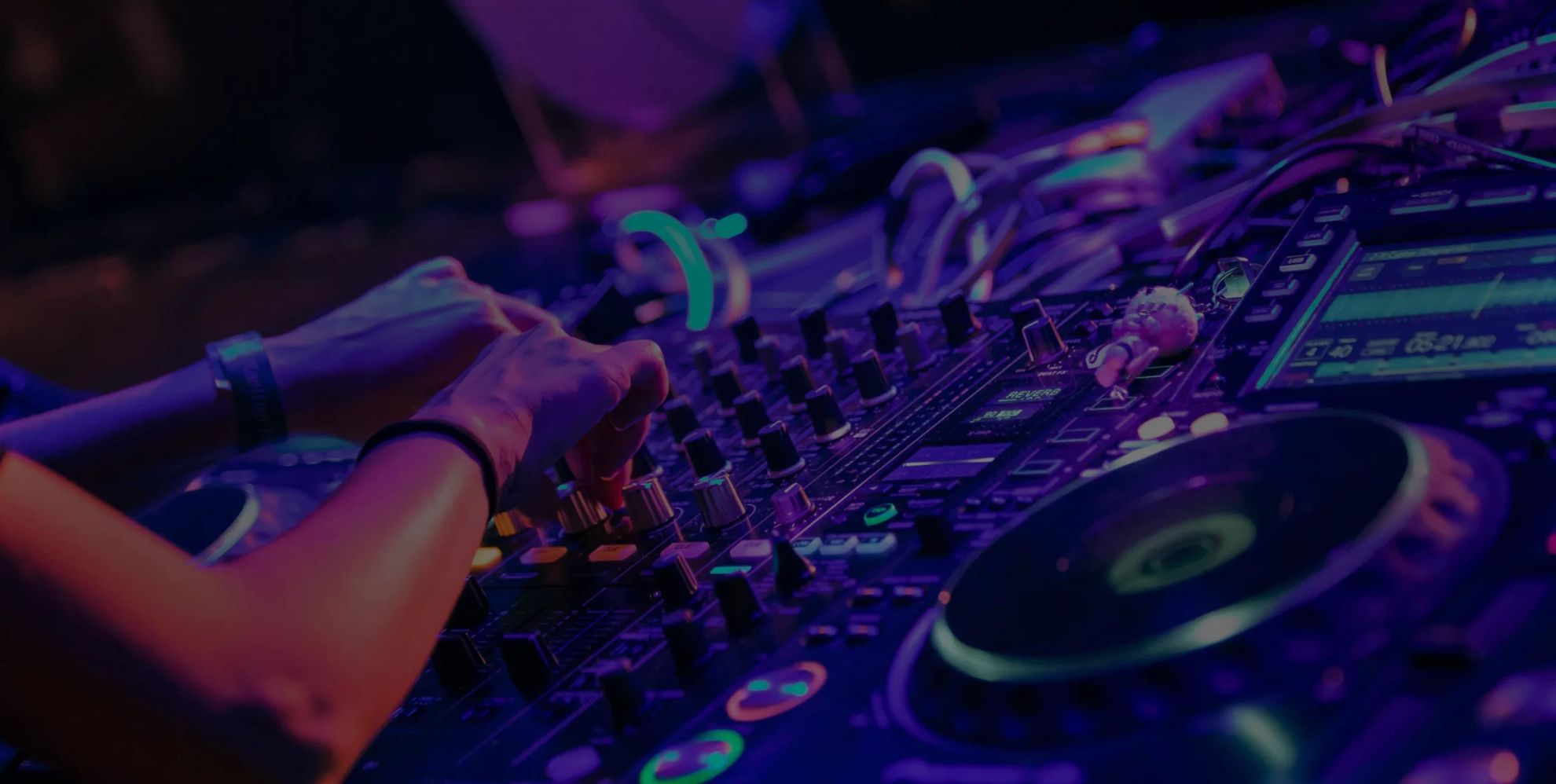 DJ hands operating a professional mixing console under purple and blue stage lighting