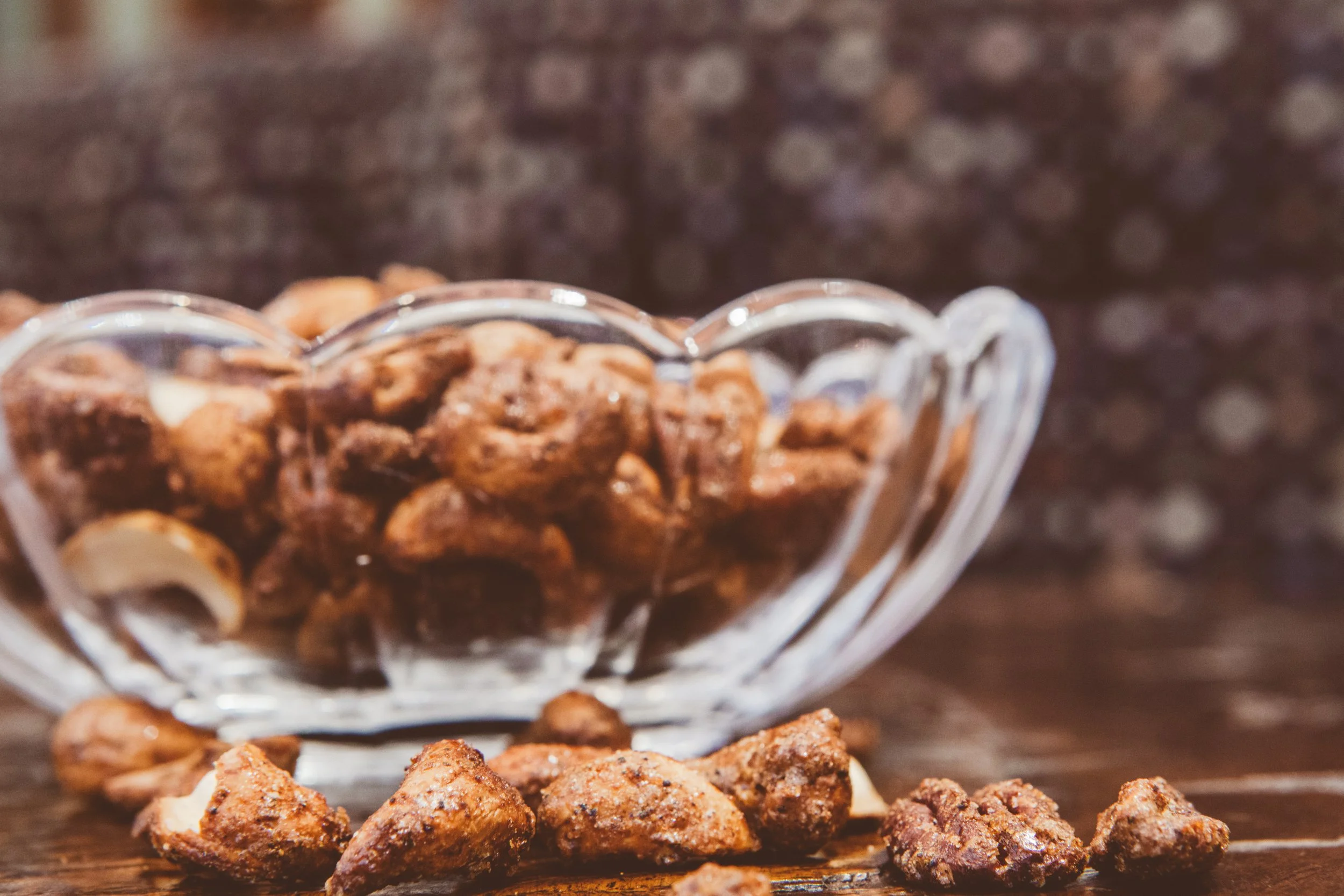 A glass bowl filled with spiced mixed nuts on a wooden surface, warm bokeh in the background.