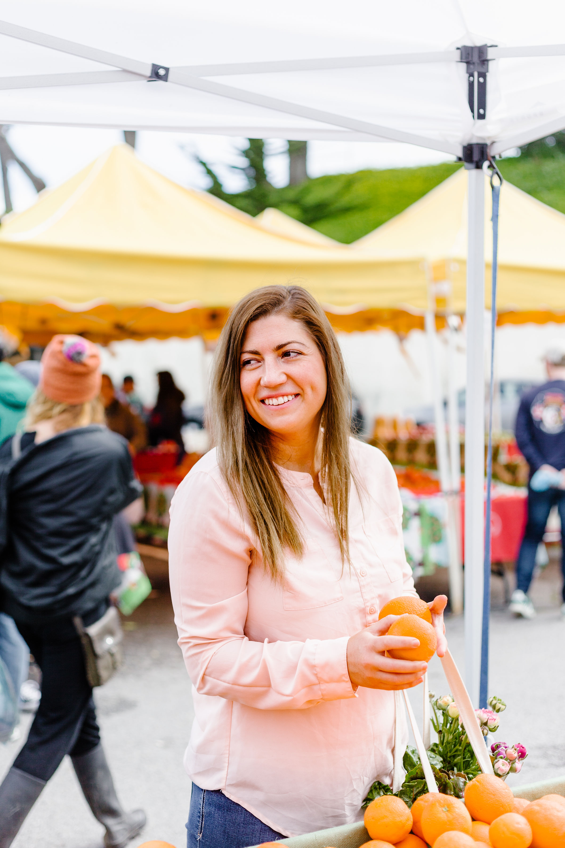 Hayley smiling and holding an orange at a farmers market