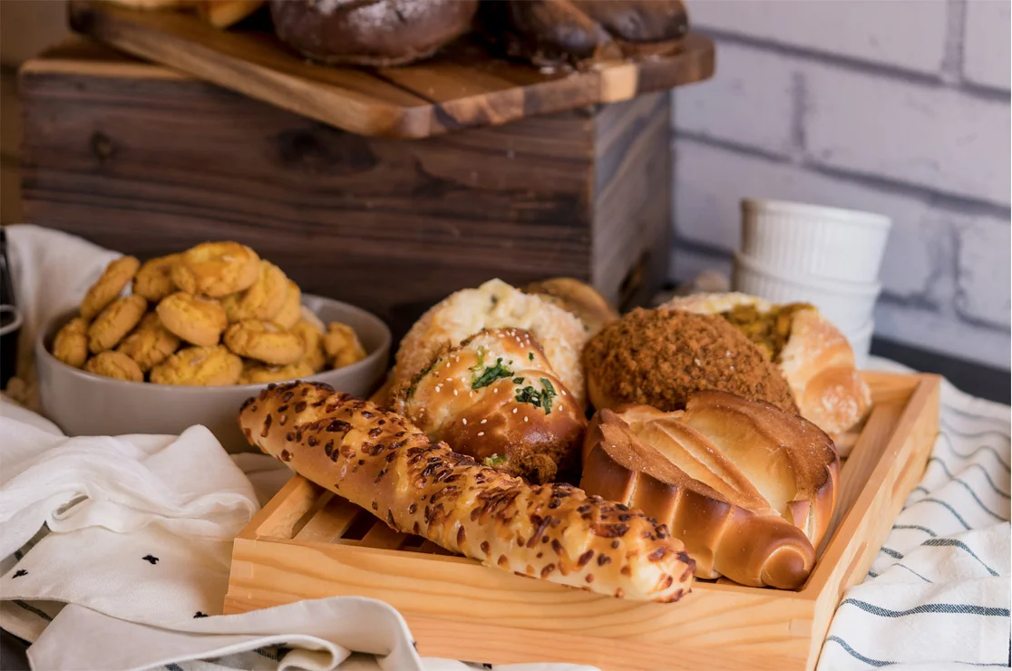 Wooden tray of assorted savory and sweet bread rolls with cookies and a rustic crate behind
