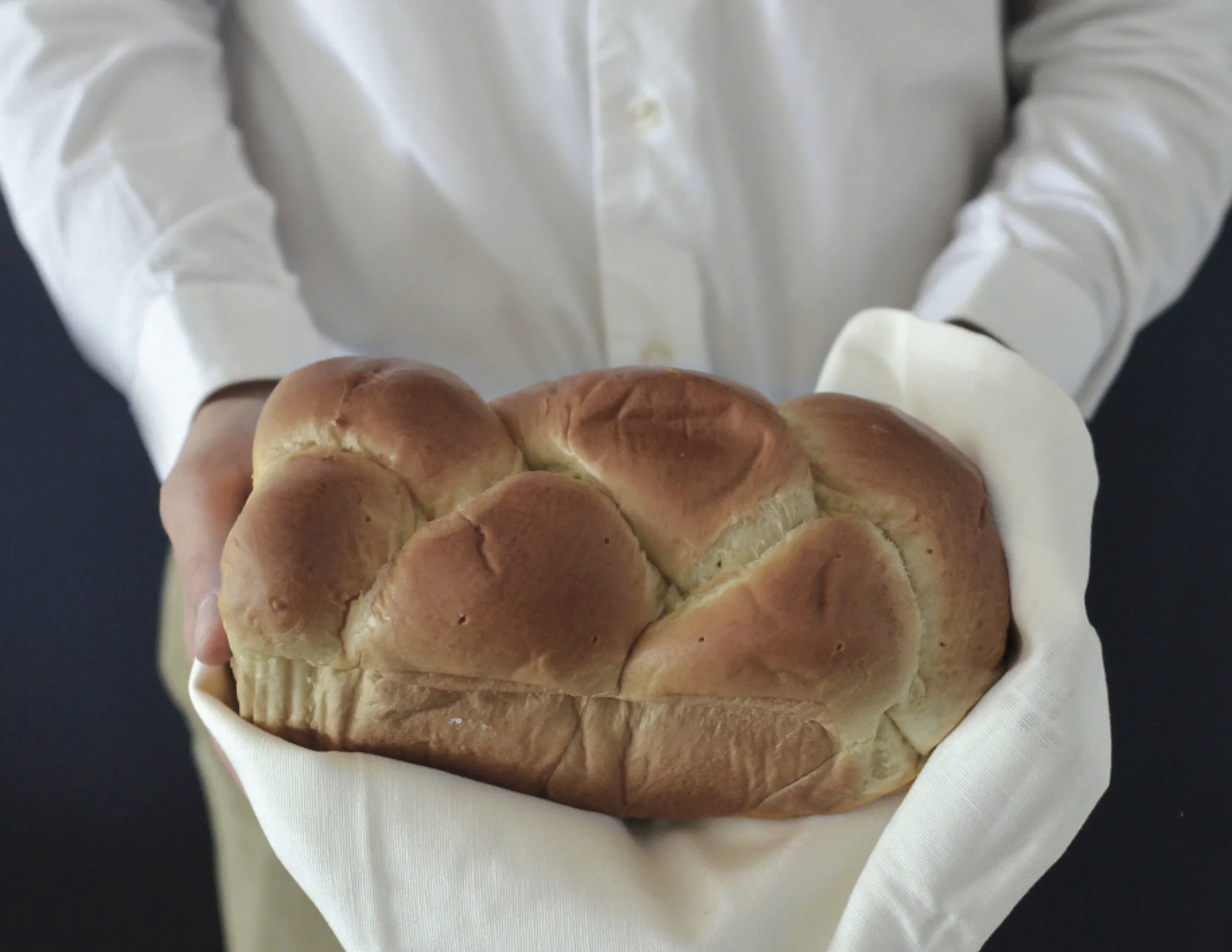 A baker in a white shirt cradling a fluffy Japanese milk bread loaf wrapped in white cloth