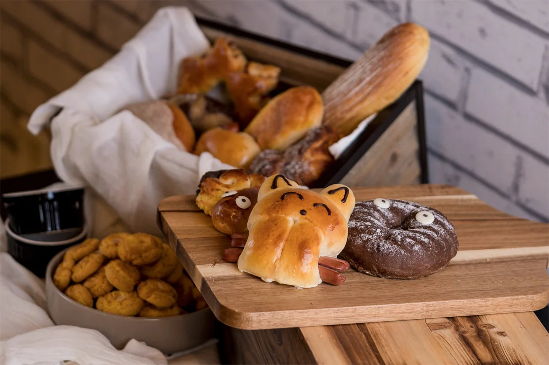 Novelty animal-shaped bread buns and pastries on a wooden board against a brick wall