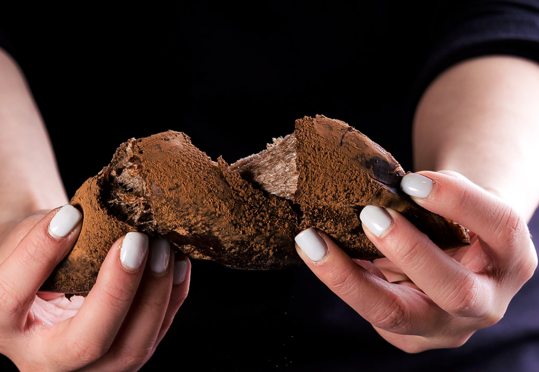 Two hands pulling apart a chocolate-dusted bread roll against a black background