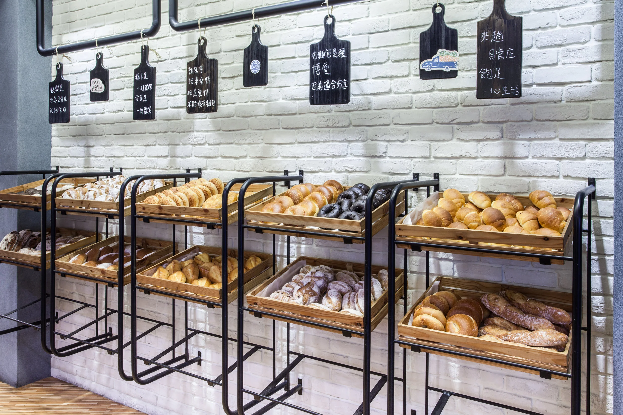 The bakery floor: rows of bread-filled wooden trays on black racks against a white brick wall with hanging Chinese signage