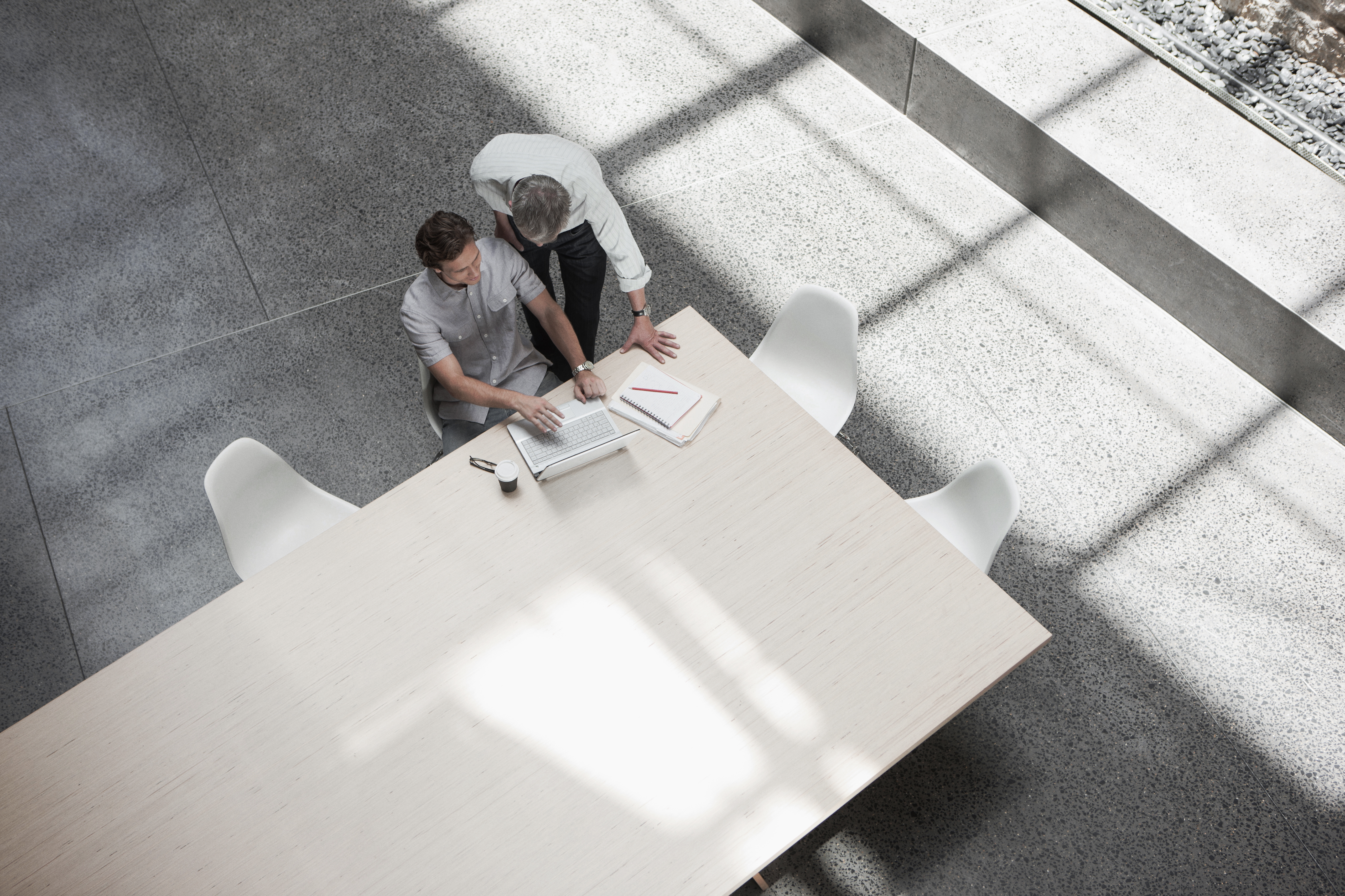 Overhead view of two colleagues working at a laptop at a light wood conference table