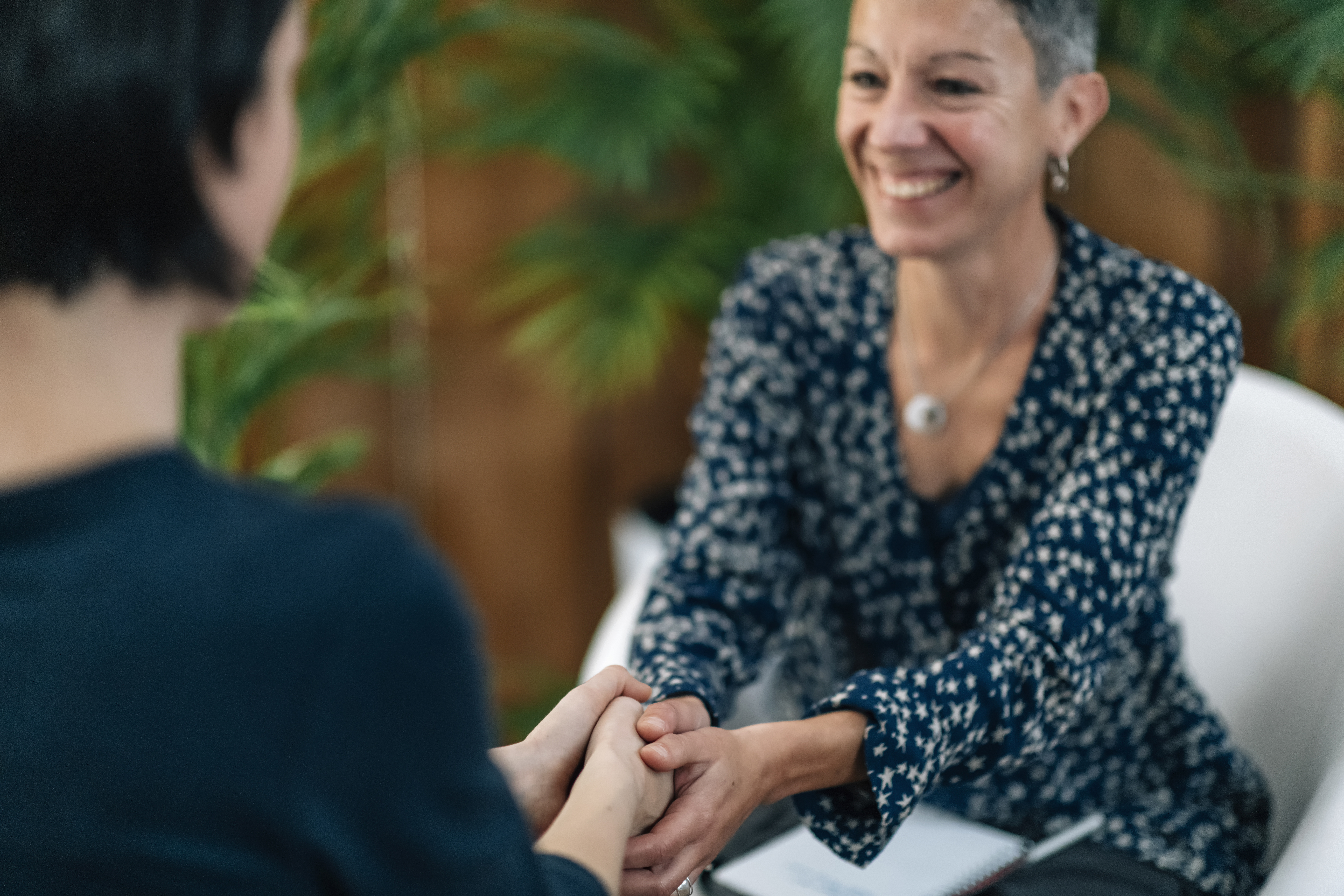 A smiling woman with short grey hair holding another person's hands during a listening-first session