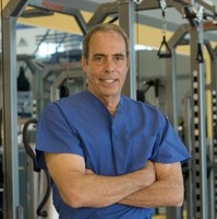 A practitioner in blue scrubs standing with arms crossed