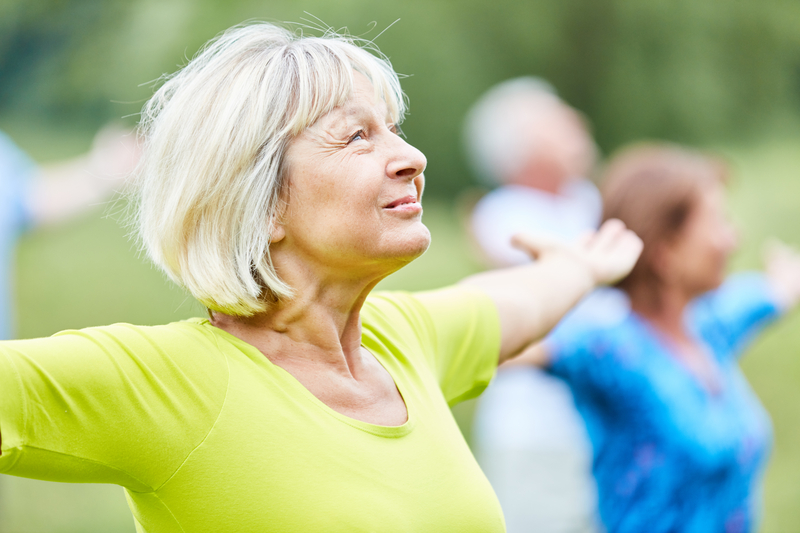 An older woman stretching with arms outstretched in an outdoor movement class
