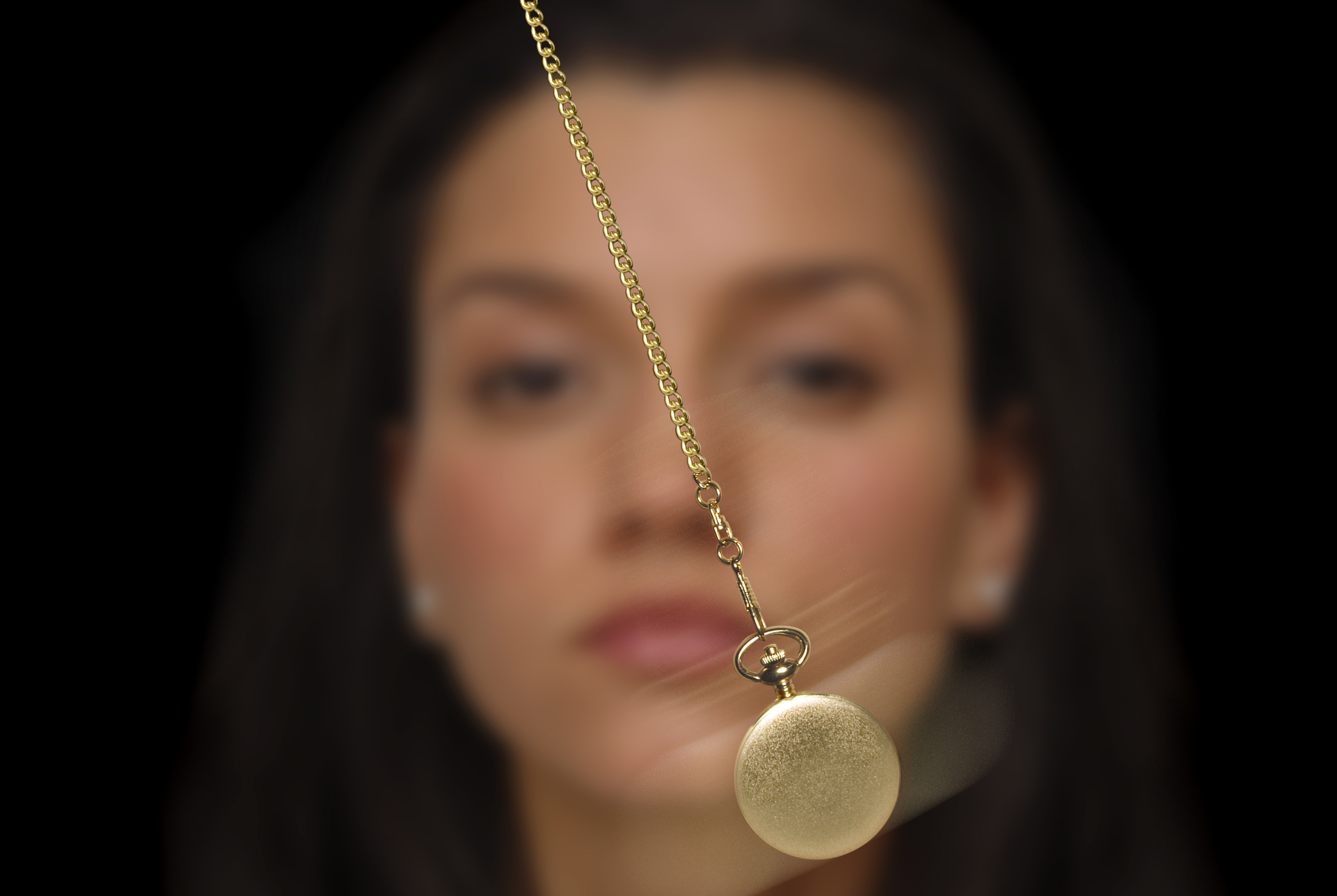 A woman watching a swinging gold pocket watch during a hypnosis session